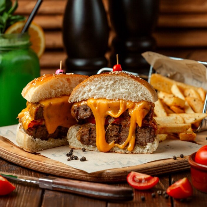 a meat burger with fried potatoes and tomato slices scattered around