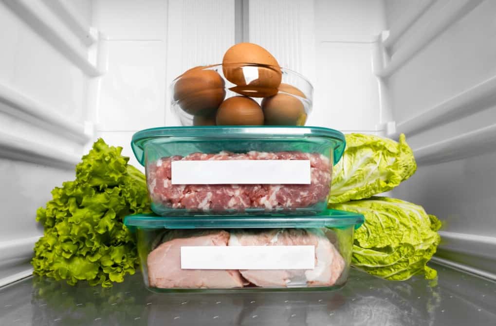 Containers of ground meat and eggs in a fridge alongside lettuce
