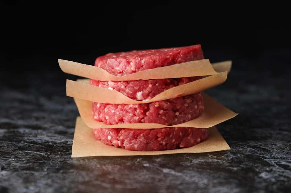Two raw burger patties separated by paper strips on a dark surface
