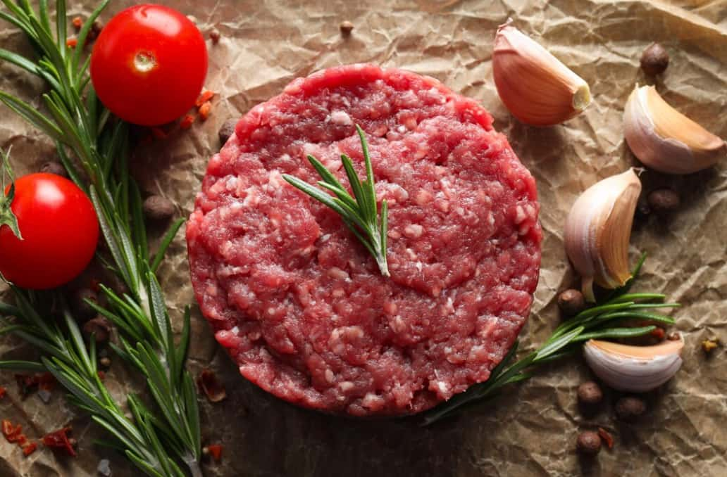 A raw hamburger patty with herbs and spices on parchment