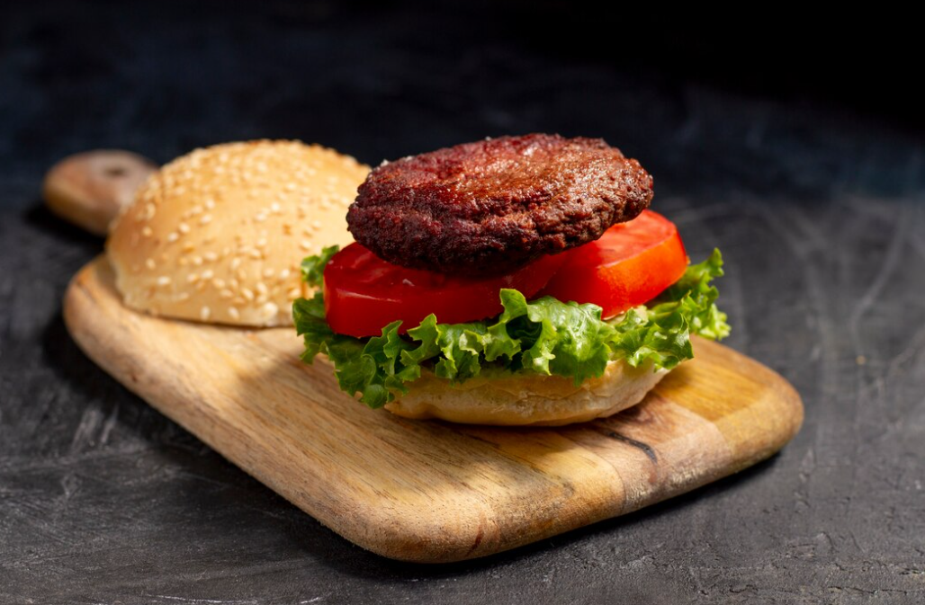 A raw burger patty on a wooden board with ingredients around
