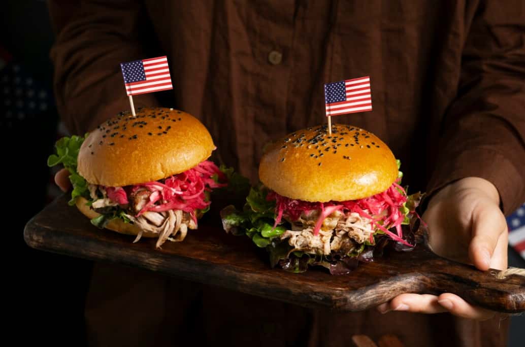 Two hamburgers with American flags on a wooden platter held by a person